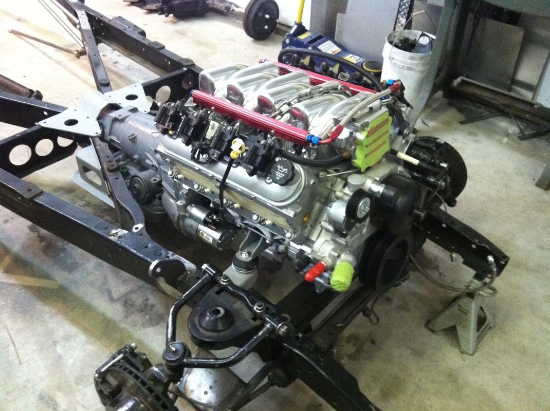 A car engine is sitting on a chassis in a garage
