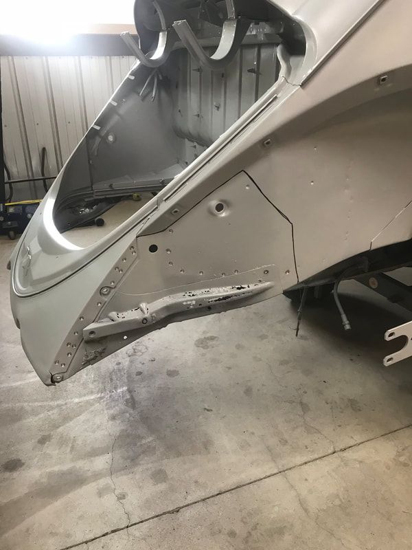 The hood of a car is sitting on the ground in a garage.