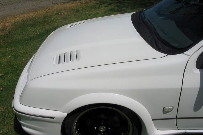 A white car with black wheels is parked in the grass