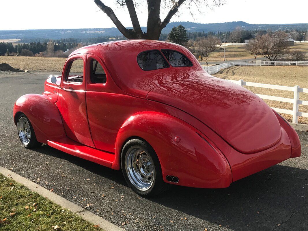 A red car is parked on the side of the road next to a tree.