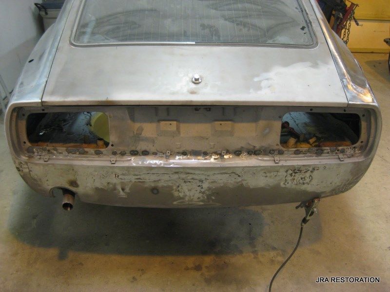 A silver car is sitting in a garage with the trunk open