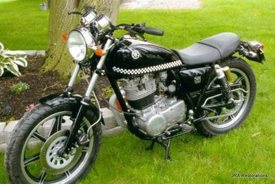 A black motorcycle is parked in the grass near a tree