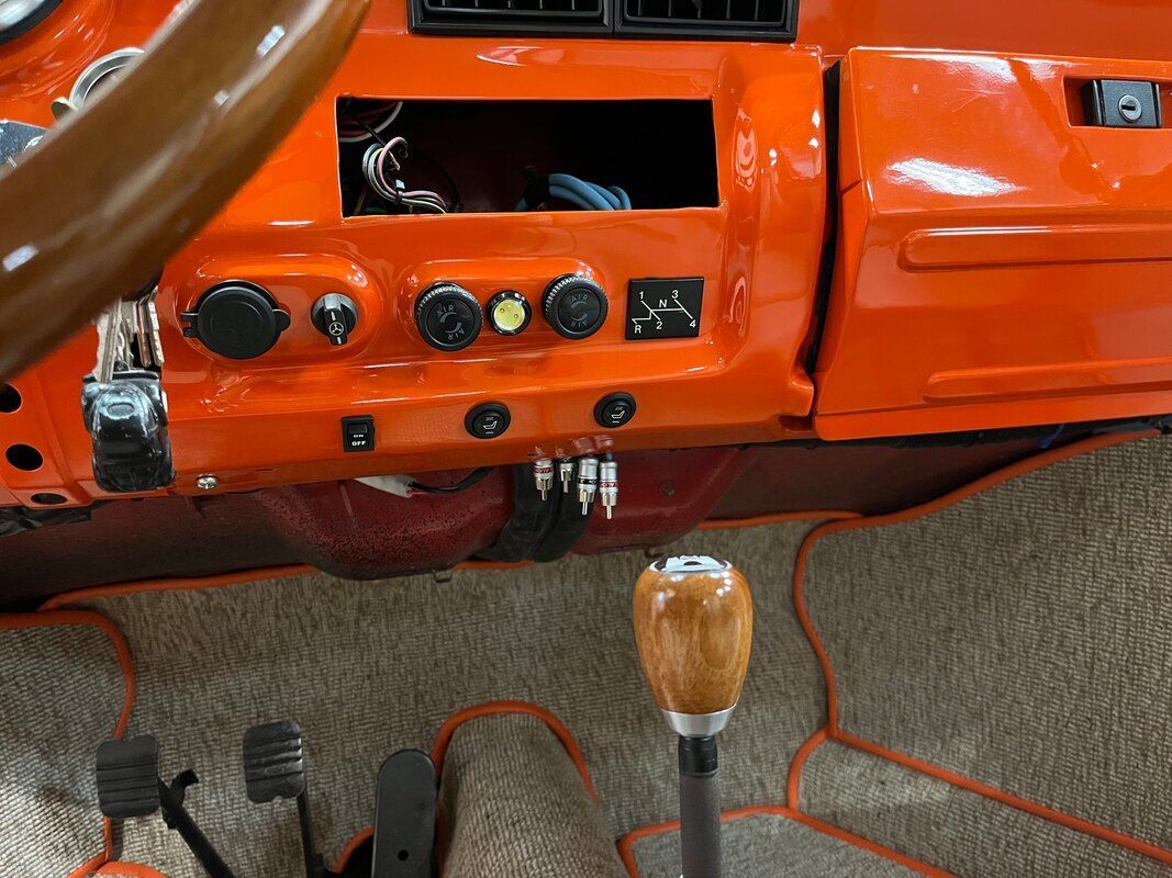 A close up of the dashboard of an orange car with a wooden shifter.