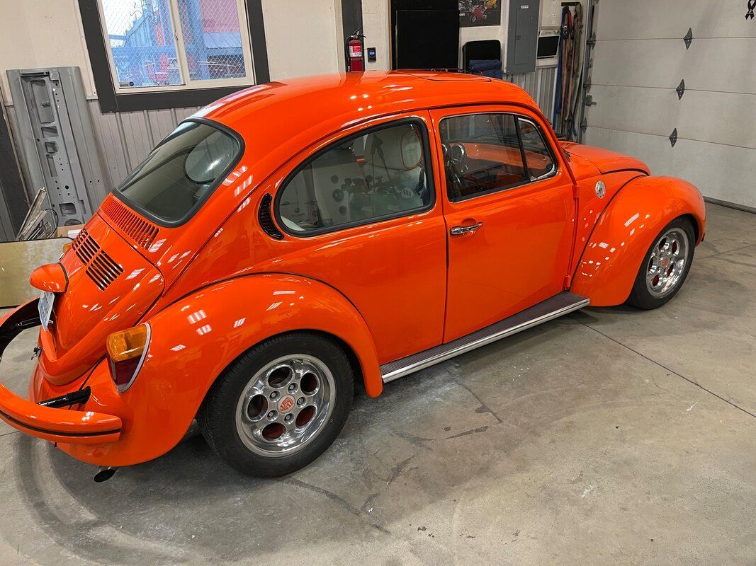 An orange volkswagen beetle is parked in a garage.