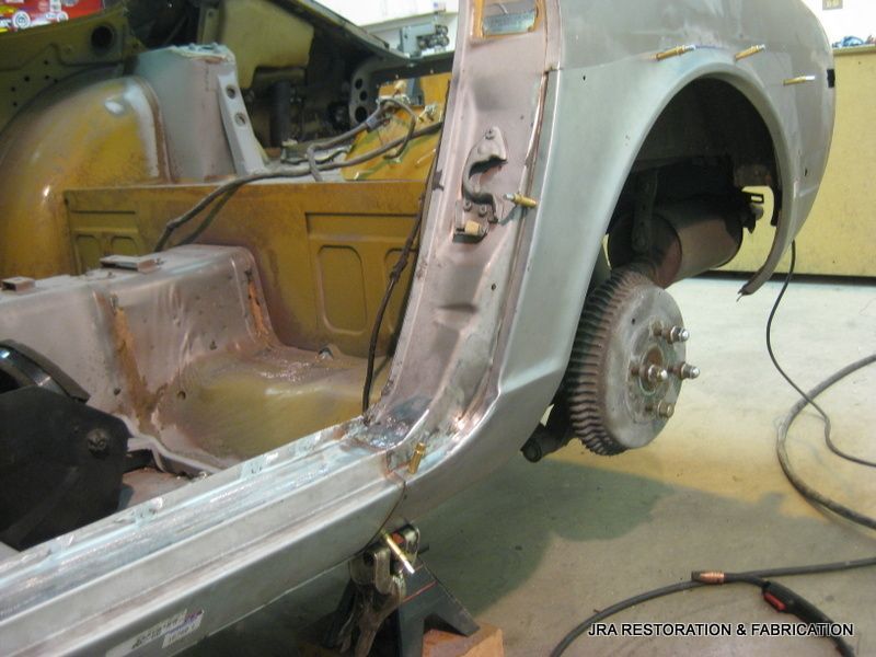 A car is being worked on in a garage with the rear wheel removed