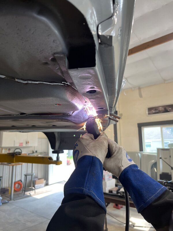 A person is welding under a car in a garage