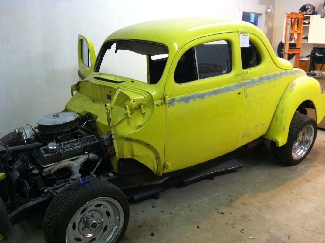 A yellow car with the engine removed is sitting in a garage