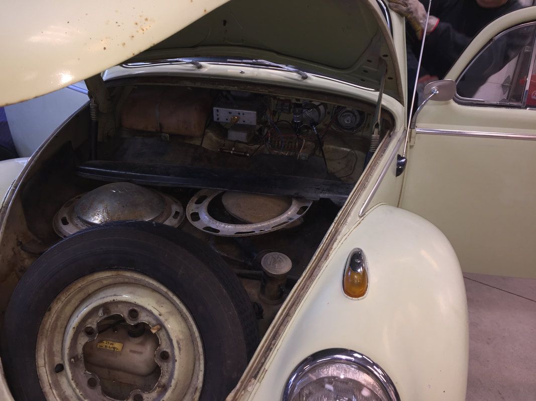 A yellow car with the hood open has a spare tire in the back