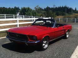 A red mustang convertible is parked in front of a white fence.