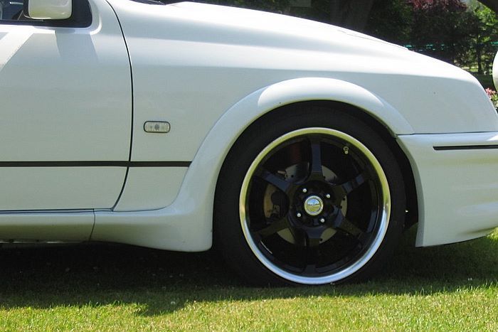 A white car with black wheels is parked in the grass