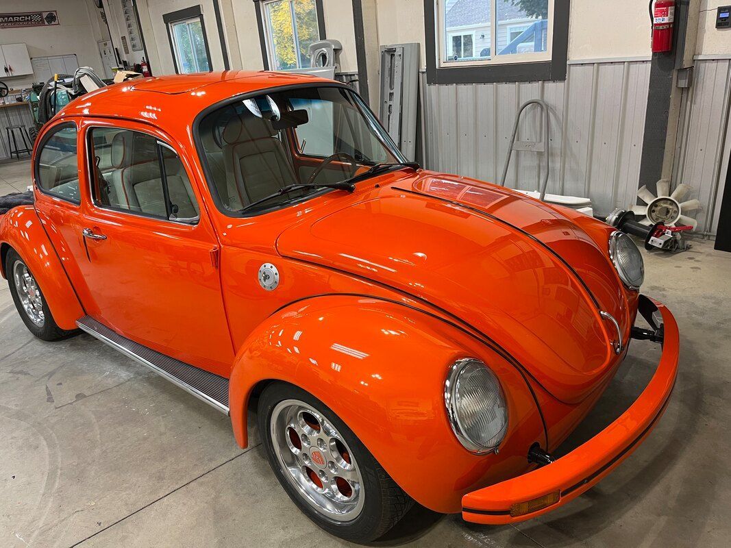 An orange volkswagen beetle is parked in a garage.
