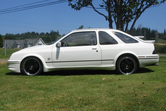 A white car with black wheels is parked in the grass