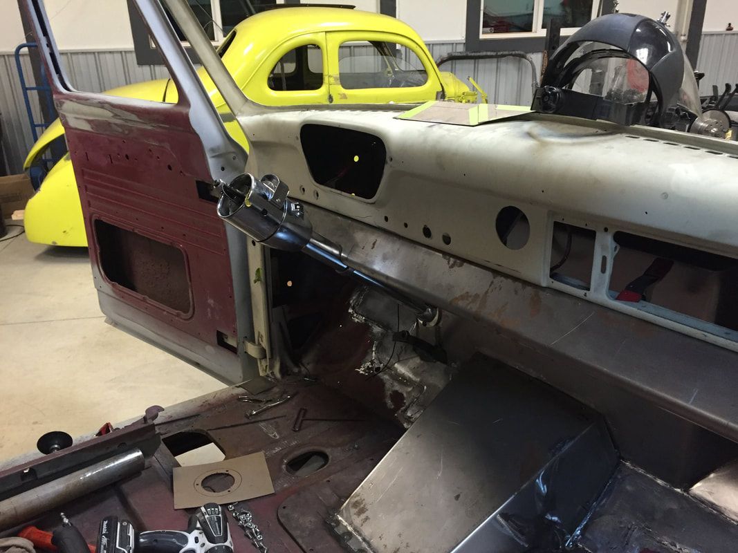 A car is being built in a garage with a yellow car in the background.