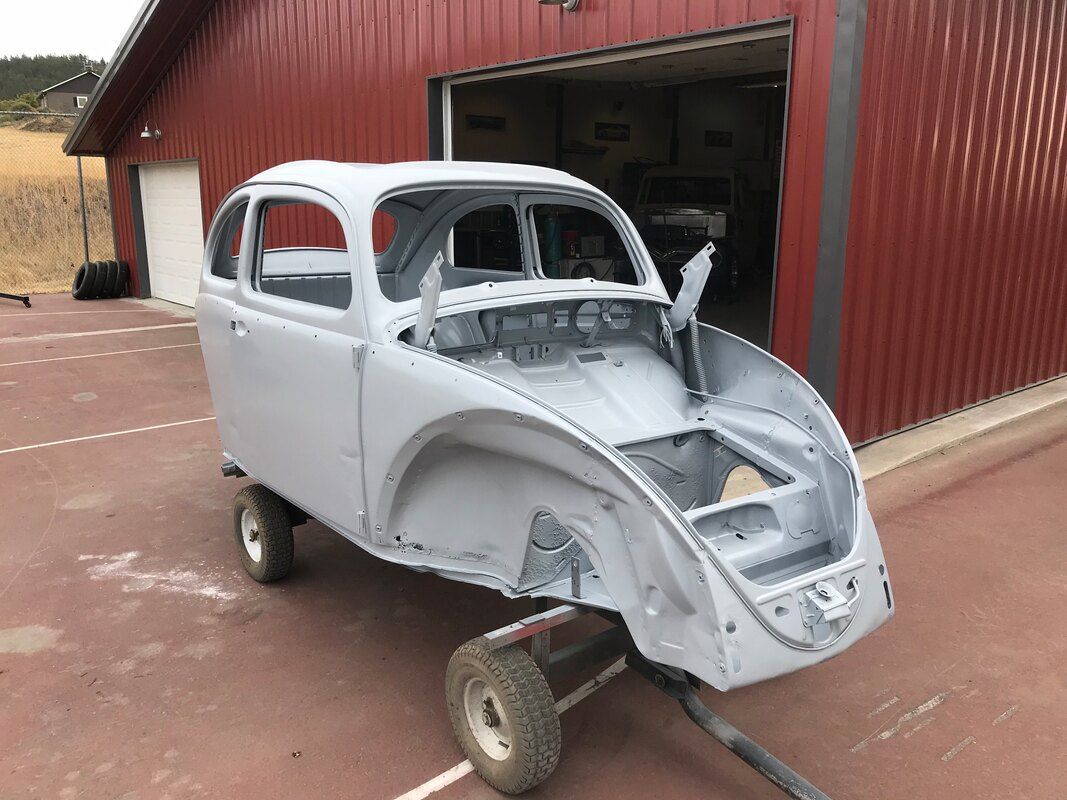 A white car is sitting on a trailer in front of a red building.