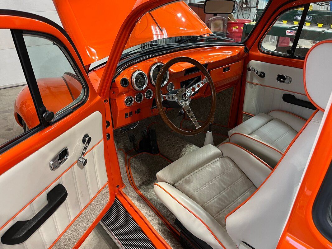 The interior of an orange car with white seats and a wooden steering wheel.
