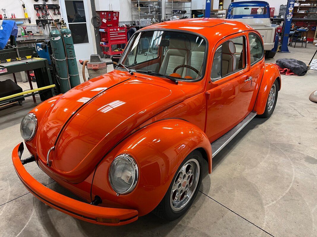 An orange volkswagen beetle is parked in a garage.
