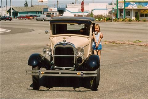 A little girl is standing in front of an old car