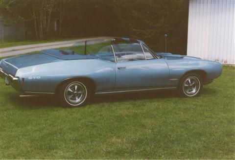 A blue convertible car is parked in the grass in front of a white building.
