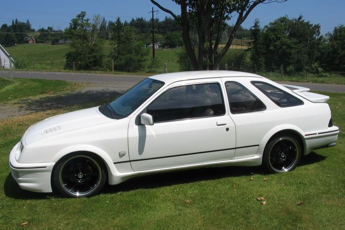 A white car with black wheels is parked in the grass