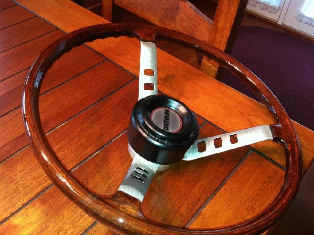 A wooden steering wheel sits on a wooden table