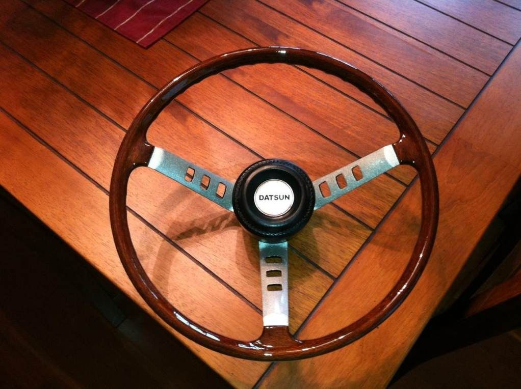 A wooden steering wheel sits on a wooden table