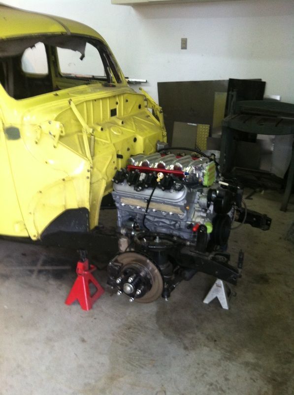 A yellow car with a engine sitting on a jack stand
