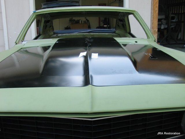 A green car with a black hood is parked in a garage