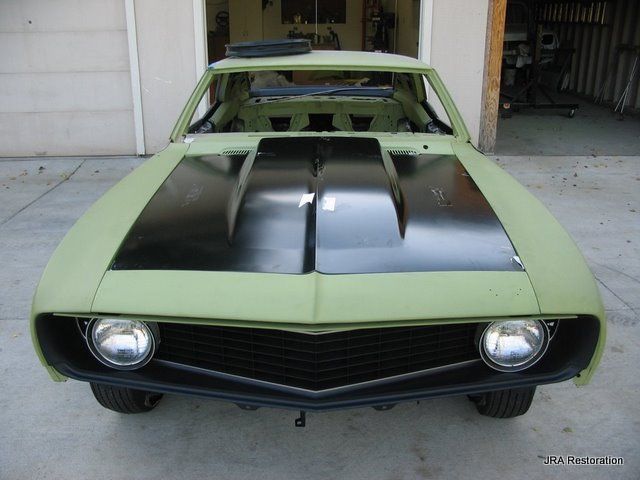 A green car with a black hood is parked in a garage