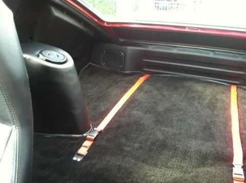 The back seat of a car with a black carpet and orange straps