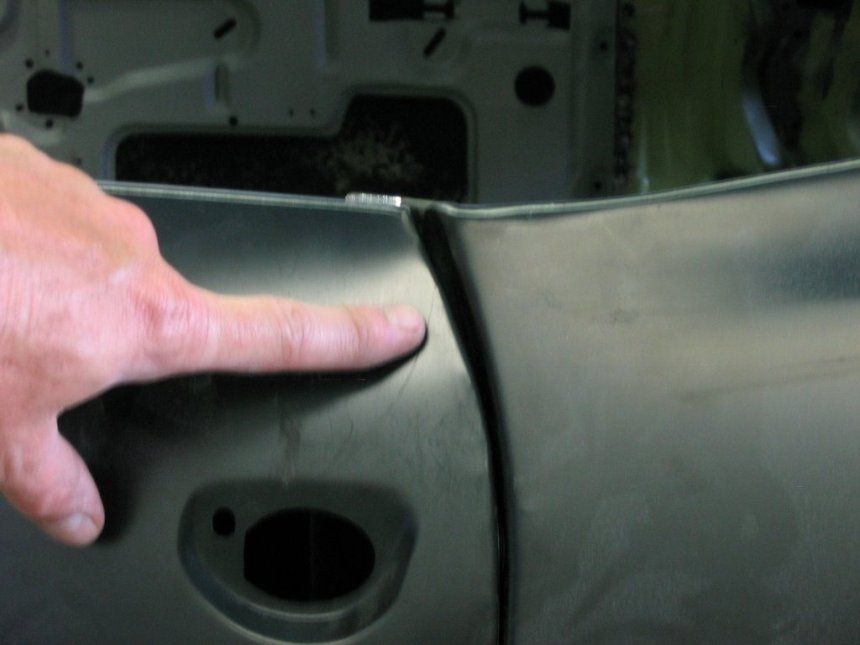 A person is pointing at a hole in a car door