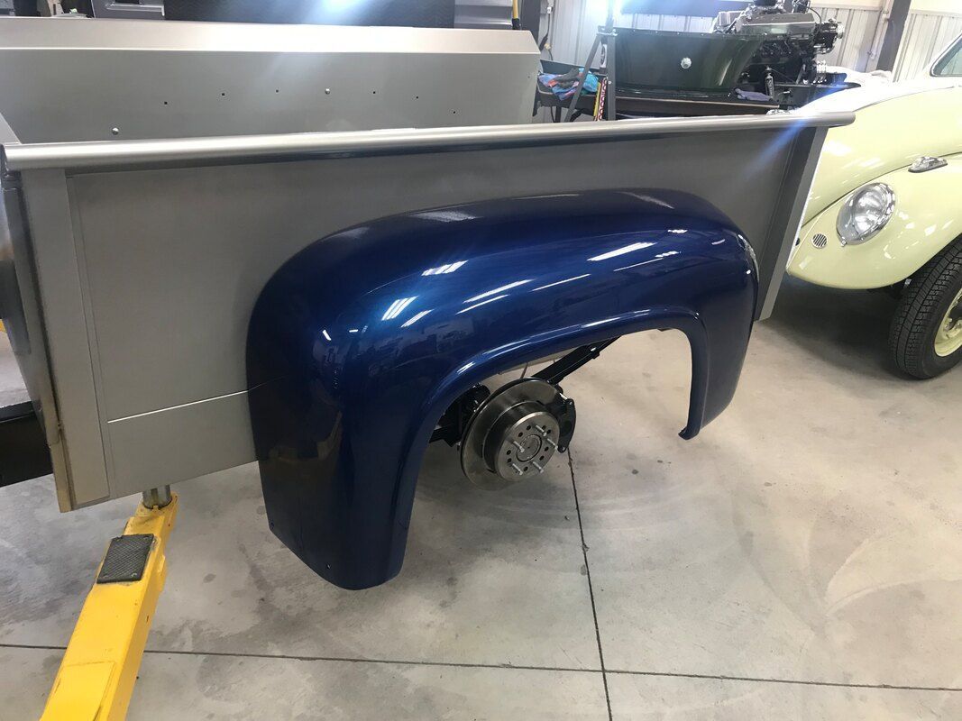 A blue truck fender is sitting on a yellow lift in a garage.