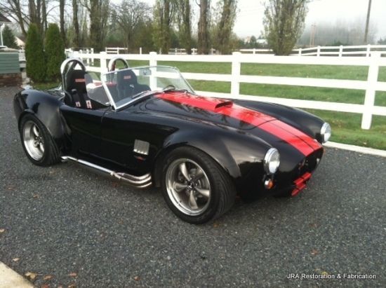 A black sports car with a red stripe on the side is parked in front of a white fence
