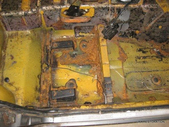 The bottom of a yellow car is covered in rust.