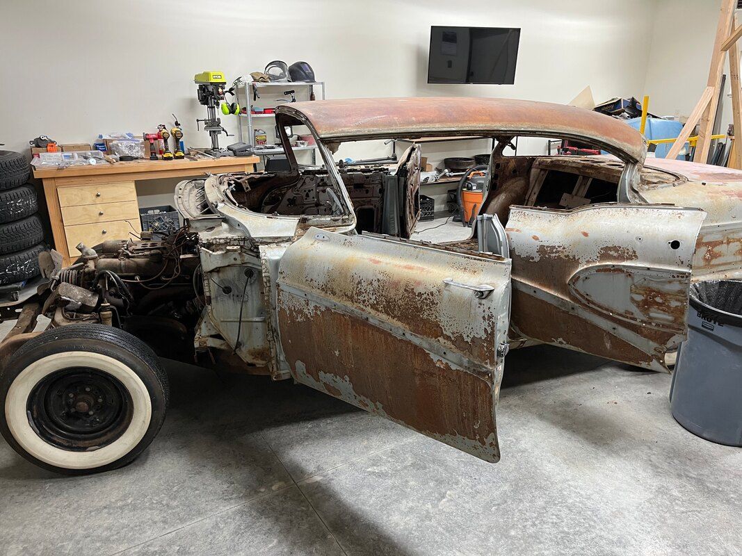 An old rusty 1958 Buick Roadmaster is sitting in a garage with its door open.