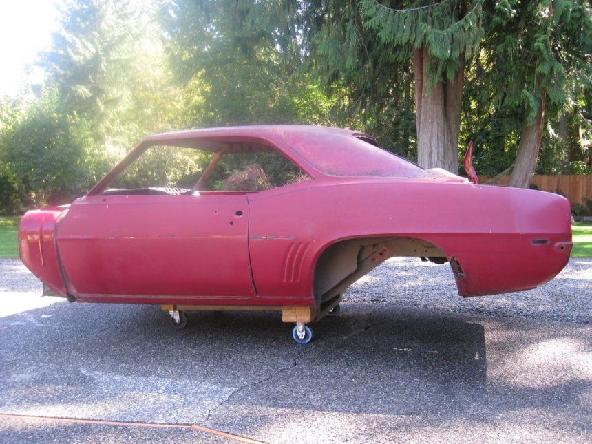 A red car is sitting on a wooden cart in a driveway.