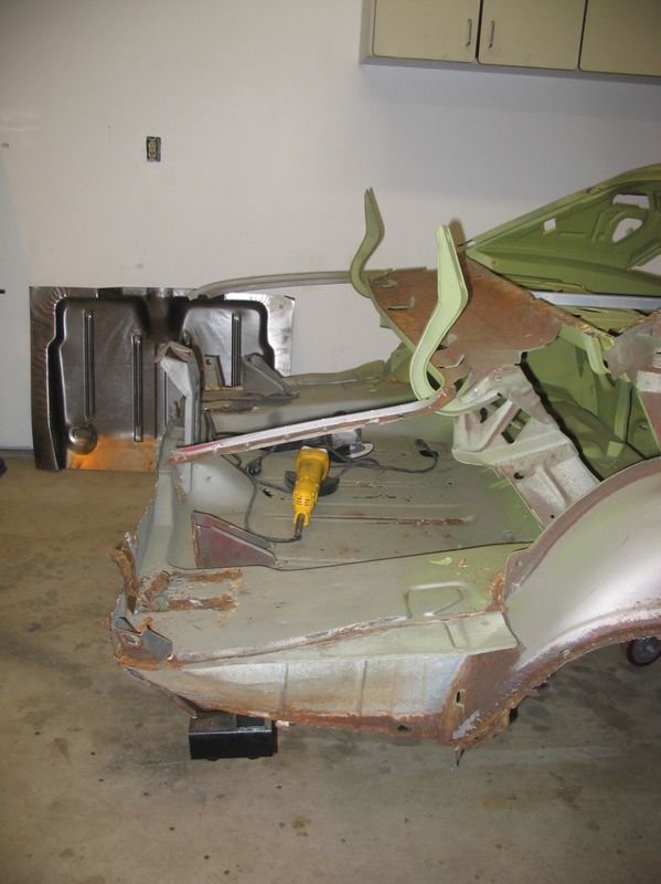 A car is being dismantled in a garage with a yellow drill.