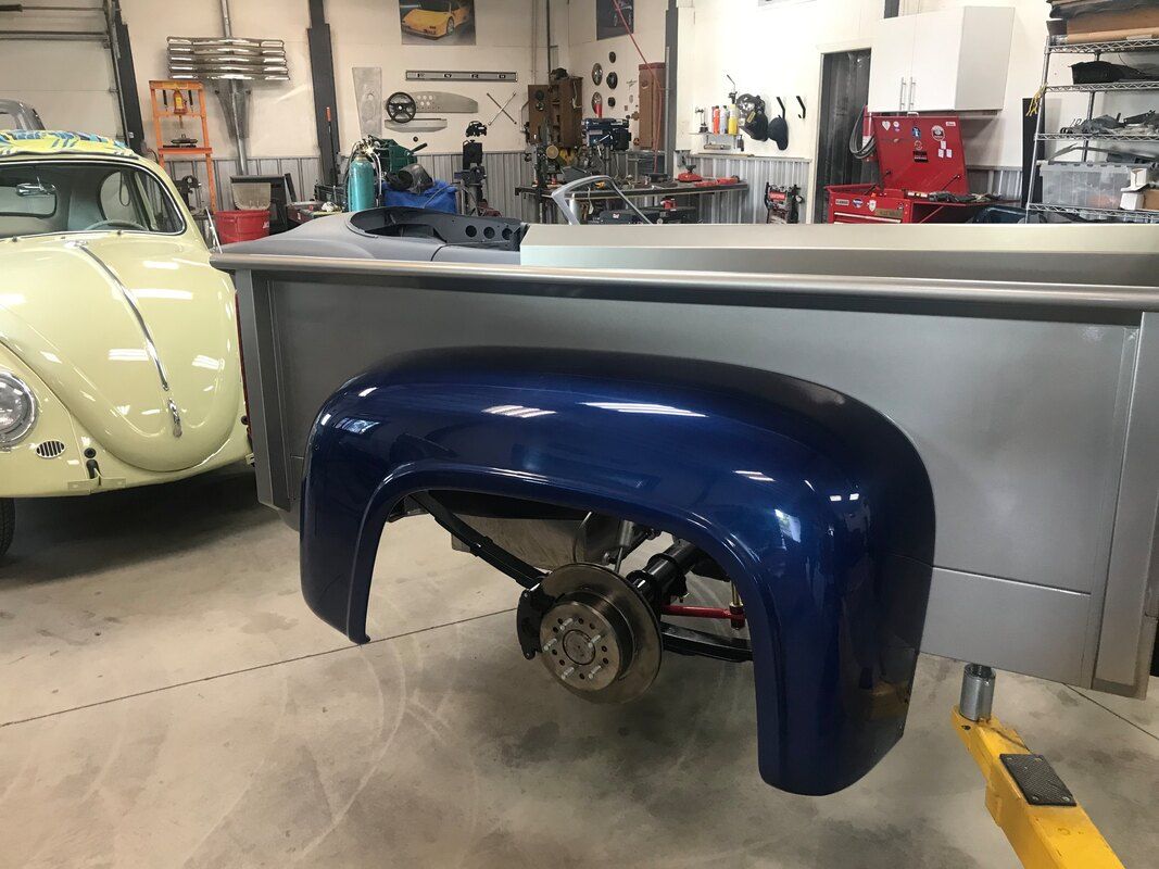 A blue fender is sitting on top of a table in a garage next to a yellow car.