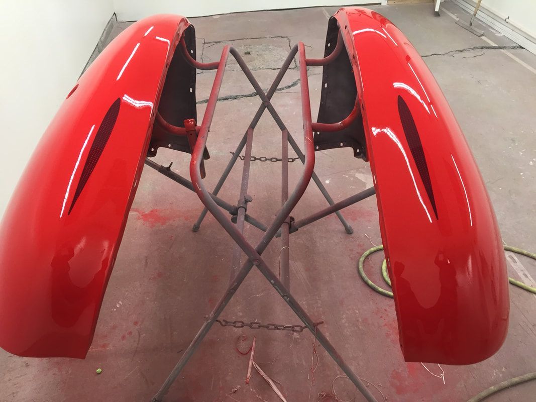 Two red fenders are sitting on a stand in a garage.