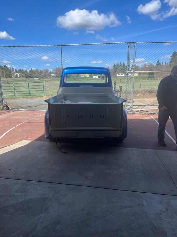A man is standing next to a blue ford truck