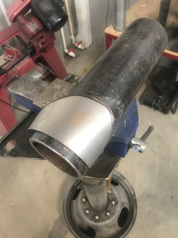 A large metal pipe is sitting on top of a wheel on a vise.