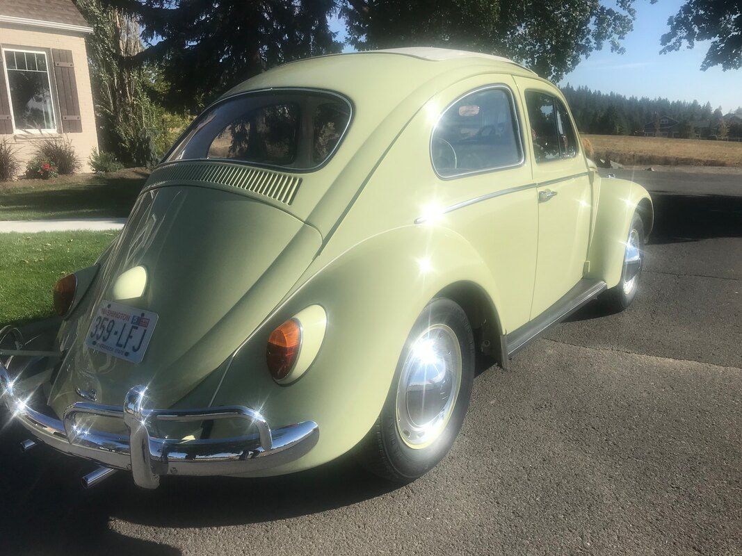 A green volkswagen beetle is parked on the side of the road in front of a house.