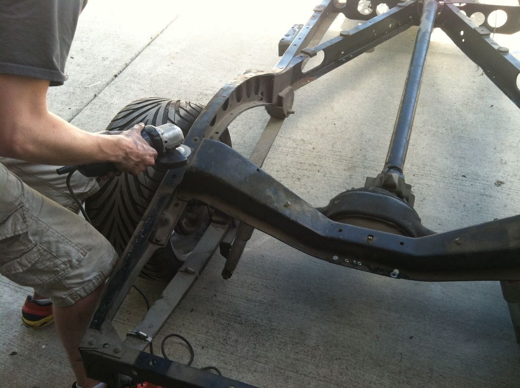 A man is working on a vehicle frame with a drill