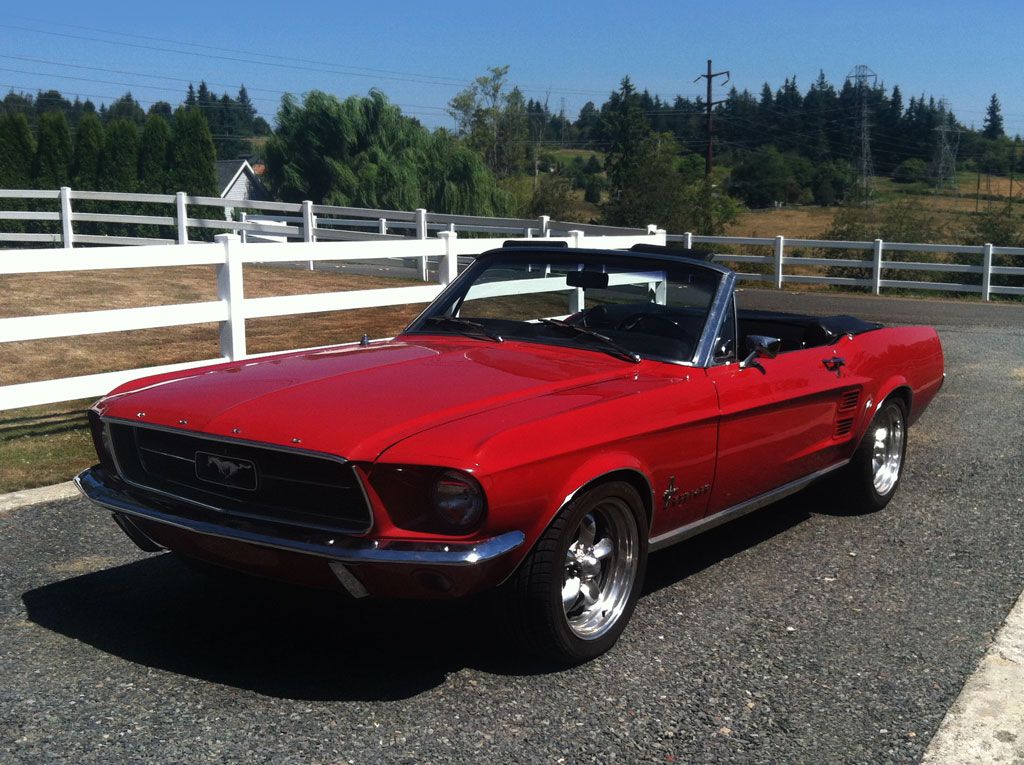 A red mustang convertible is parked in front of a white fence.