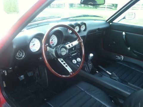 The interior of a red sports car with a wooden steering wheel