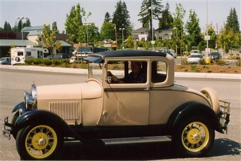 An old car with yellow wheels is parked in a parking lot