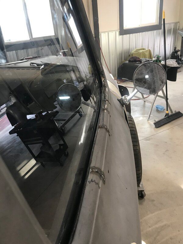 A car is sitting in a garage with a fan and a broom.