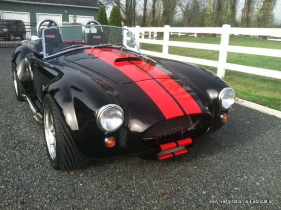 A black car with red stripes is parked in front of a white fence