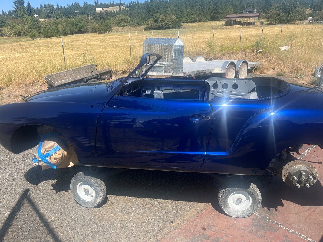 A blue car is parked on the side of the road in a field.