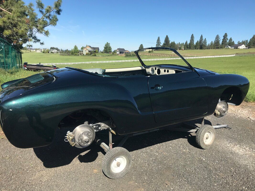 A green convertible car is parked on a gravel road.