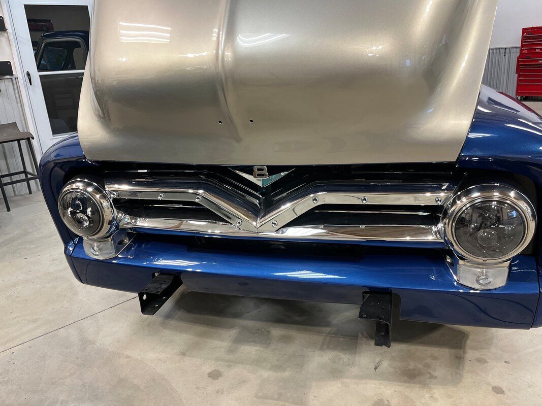 A blue car with the hood up is sitting in a garage.